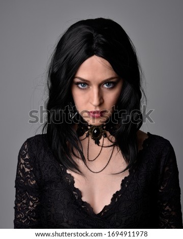 Close up portrait of a pretty, goth girl with dark hair  posing in front  a studio background.