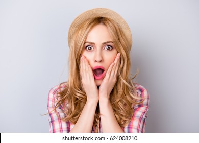 Close up portrait of pretty surprised woman with opened mouth in hat and checkered shirt isolated on gray background
