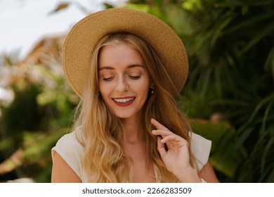  Close up portrait of Pretty traveling   blond woman in straw hat posing  in trpical stylish hotel. White summer clothes. Perfect wavy hairs.  - Powered by Shutterstock