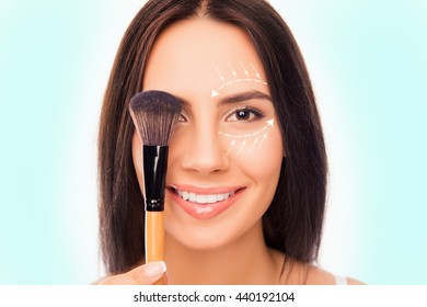 Close up portrait of pretty woman holding makeup brush near eye with arrows