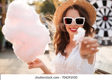 Close up portrait of a pretty young girl in sunglasses eating cotton candy at amusement park