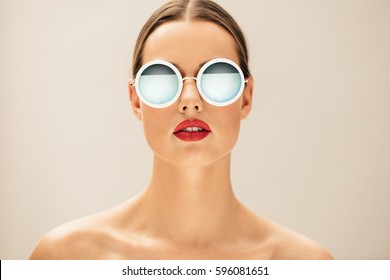 Close up portrait of pretty young woman with glasses against beige background. Female fashion model posing with sunglasses.