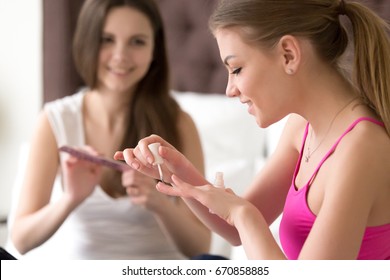 Close up portrait of pretty young woman painting nails with her girlfriend on blurred background using nail file. Female friends do manicure procedures when spending time together and chatting at home - Powered by Shutterstock