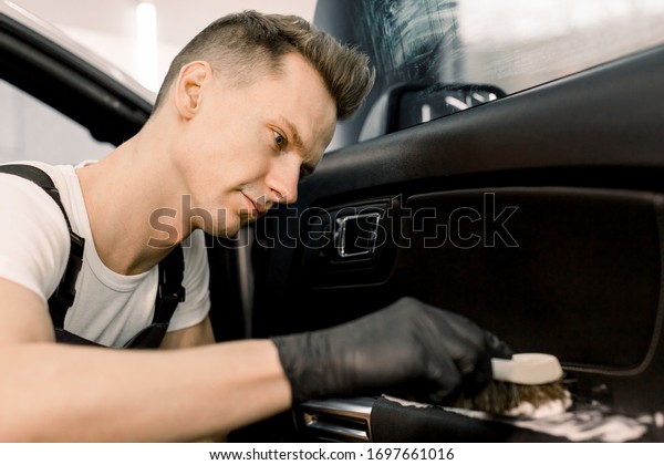 Close up\
portrait of professional car wash service worker in black\
protective gloves, cleaning car interior with special chemical foam\
and soft brush. Selective focus on worker\
face