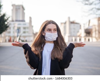 Close Up Portrait Of Puzzled Woman Shrugging Shoulders Wearing Medical Mask Holding Hands In Air In Confusion With The Face Expression I Do Not Know Standing In A City. Protection From Coronavirus.