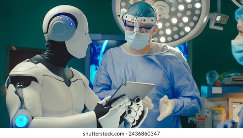 Close up portrait Robot holding digital tablet helps doctor to perform surgical operation in modern hospital. Teamwork of professional medical surgeons in operating room. - Powered by Shutterstock