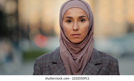 Close up portrait sad upset female face pensive serious muslim business woman young islamic girl ethnic lady wearing hijab stands in city looks away looking at camera religious discrimination concept - Powered by Shutterstock