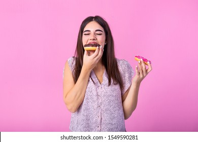 Close up portrait of a satisfied pretty girl eating donuts isolated over pink background. Young happy caucasian girl eating chocolate donuts in front of pink wall