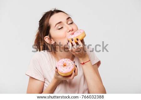 Close up portrait of a satisfied pretty girl eating donuts isolated over white background