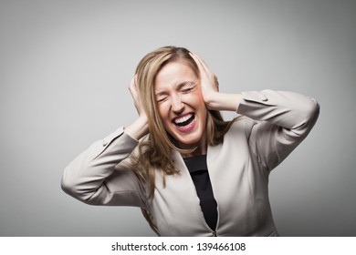 Close up portrait of a screaming young businesswoman covering ears with her hands isolated on grey background