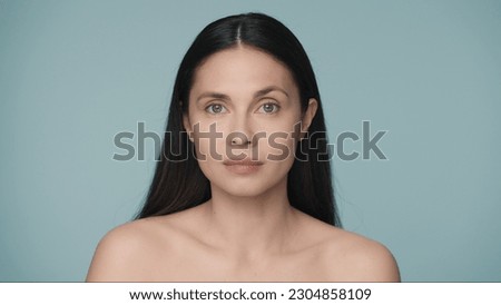 Close up portrait of a seminude woman on a blue background. A woman with natural make up looks straight ahead. Beauty concept. Natural beauty, cosmetology, skin care.