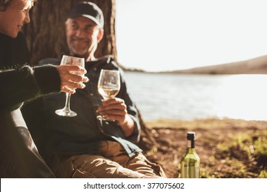 Close up portrait of senior couple drinking wine while camping near a lake. Focus on hands holding glass of wine. - Powered by Shutterstock