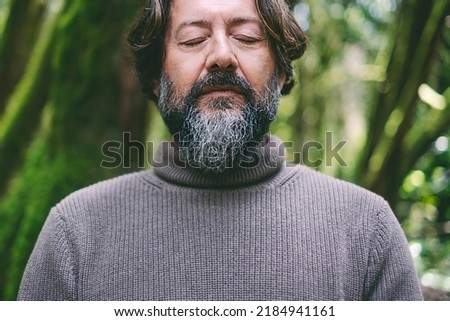 Close up portrait of senior map with closed eyes in inner balance serene meditation alone with green forest nature in background. Positive lifestyle for healthy people. Earth's day concept lifestyle
