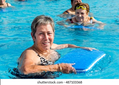 Close up portrait of senior woman doing water exercise with kicking board in outdoor pool.