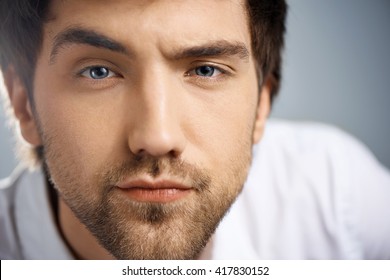Close up portrait of serious elegant handsome young businessman in white shirt looking at camera raising one eyebrow. Studio, isolated on grey background.
