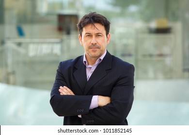 Close Up Portrait Of Serious Older Man In Business Suit Standing With Arms Crossed Outdoors