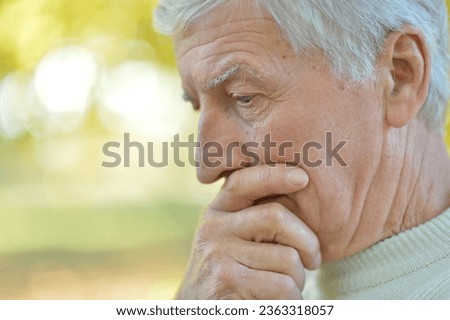 Close up portrait of serious senior man thinking in park on green background
