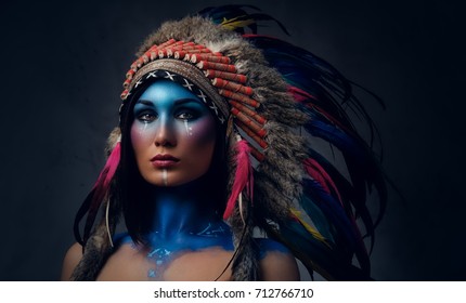 Close up portrait of shamanic female with Indian feather hat and colorful makeup.