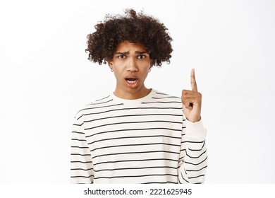 Close Up Portrait Of Shocked, Upset Young Guy Poiting Finger Up, Look Concerned And Disappointed By Smth, Standing Over White Background