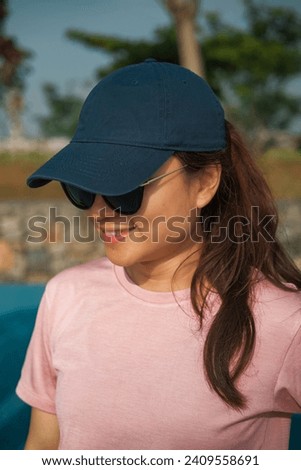 Close up portrait shot of sporty asian young woman wearing black sport sun glasses and blue navy hat with pink running jersey. Sport, healthy, wellbeing lifestyle concept.