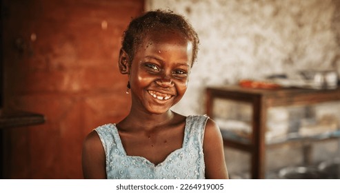 Close Up Portrait of a Shy Authentic African Little Girl Smiling at the Camera with Blurred Background. Black Female Kid Representing Future, Hope, and Acceptance. Documentary Concept