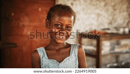 Close Up Portrait of a Shy Authentic African Little Girl Smiling at the Camera with Blurred Background. Black Female Kid Representing Future, Hope, and Acceptance. Documentary Concept