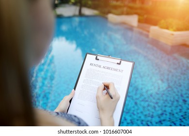 close portrait of signing rental agreement document on background of swimming pool. woman taking apartment for long term. Front used with Open Font License