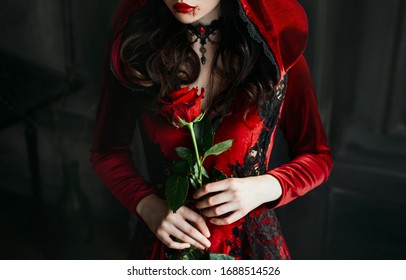 Close Up portrait silhouette gothic evil woman queen. sexy witch face. red medieval cape dress holiday costume hood. princess holding rose in hands. Vampire makeup lips dripping blood halloween image