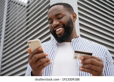 Close up portrait of smiling African man holding credit card, using modern mobile app shopping online
