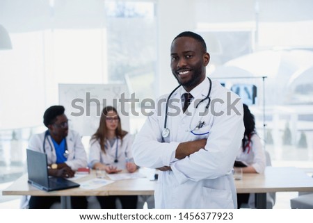 Close up portrait of smiling afro american male doctor. Medical assistant or student in white uniform with stethoscope. Handsome male doctor with a medical group at meeting room.
