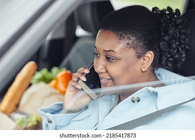 Close Up Portrait Of Smiling Black Woman Speaking On Phone In Car With Grocery Bag In Background