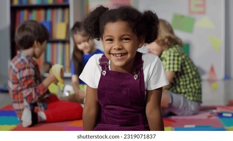 Close up portrait of smiling little African-American girl looking at camera at primary school. Adorable preschool kid sitting in playroom of kindergarten - Powered by Shutterstock