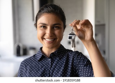 Close up portrait of smiling millennial Indian woman hold show keys to new house. Excited young ethnic female renter or buyer celebrate moving relocation to home or apartment. Rent, realty concept.