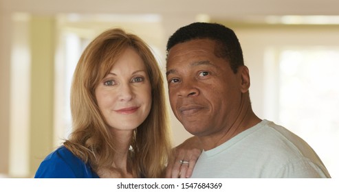 Close Up Portrait Of Smiling Mixed Race Senior Couple Looking At Camera. Happy Older African American Husband And Caucasian Wife At Home