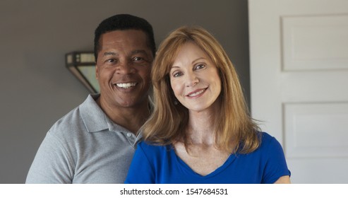 Close Up Portrait Of Smiling Mixed Race Senior Couple Looking At Camera. Happy Older African American Husband And Caucasian Wife At Home