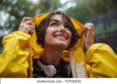 Close up portrait of a smiling pretty teenage girl with headphones wearing raincoat outdoors