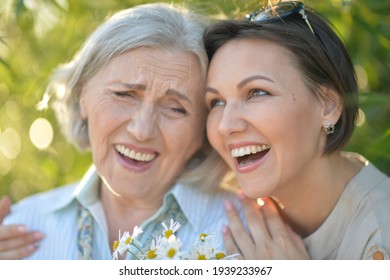 Close Up Portrait Of Smiling Senior Woman With Adult Daughter With Flowers In Park