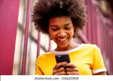 Close Up Portrait Of Smiling Young African American Woman Looking At Mobile Phone Outside