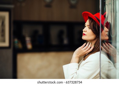 Close Up Portrait Of A Stylish Brunette Business Woman Wearing In White Coat Red Hat, Standing At The Entrance Of Hotel Or Boutique. Model Looking Aside. Female Fashion Concept. City Lifestyle.