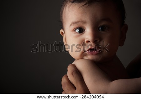 Close up portrait of a surprised indian baby boy in fathers arms looking at camera over dark gray background