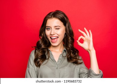 Close up portrait of sweet, gorgeous, nice, adorable, good-looking lady with modern curly hairstyle, casual shirt, show Ok sign and wink isolated on shine red background