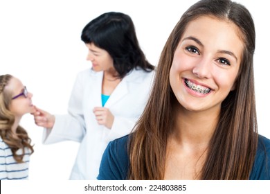 Close up portrait of Teen girl with dental braces and doctor with patient in background.Isolated on white.