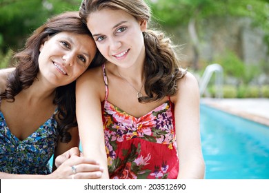 Close Up Portrait Of A Teenager Daughter And Her Mother Hugging And Smiling During A Summer Holiday Break In A Vacation Villa Green Garden And Swimming Pool, Relaxing Together. Outdoors Lifestyle.