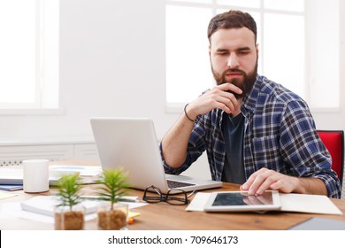 Close up portrait of a thinking young man sitting and using tablet computer in office - Shutterstock ID 709646173