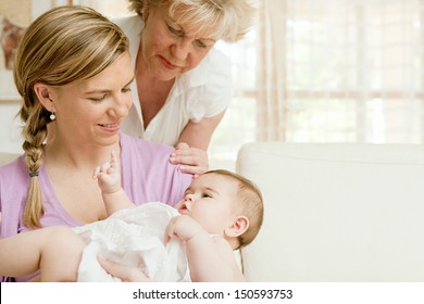 Close Up Portrait Of Three Generations Of Women Being Close, Grandmother, Mother And Baby Daughter At Home, Being Calm And Relaxing Together Around Each Other.