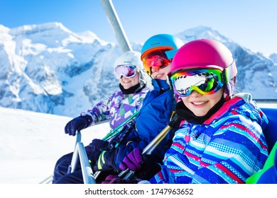 Close portrait of three smiling happy girls on chairlift on ski resort with sunny mountain peaks on background