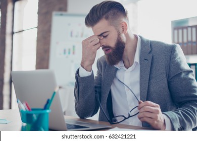 Close up portrait of tired bearded young man with strong migraine grimace. He is wearing the formalwear, holding his glasses, sitting at the workplace - Shutterstock ID 632421221