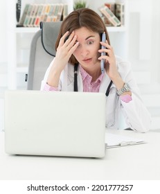 Close Up Portrait Of Tired Female Doctor Sitting At The Desktop And Talking To Phone In The Office Of Modern Clinic