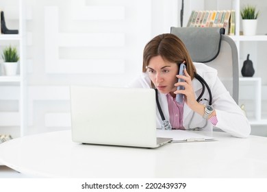 Close Up Portrait Of Tired Female Doctor Sitting At The Desktop And Talking To Phone In The Office Of Modern Clinic