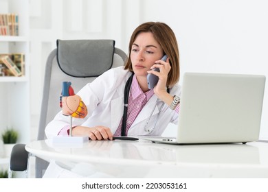 Close Up Portrait Of Tired Female Doctor Sitting At The Desktop And Talking To Phone In The Office Of Modern Clinic	